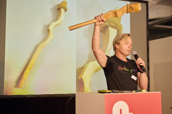 A photo of Mike holding up stick about as long as a baseball bat, but with some curves and a rubber hose over its end.