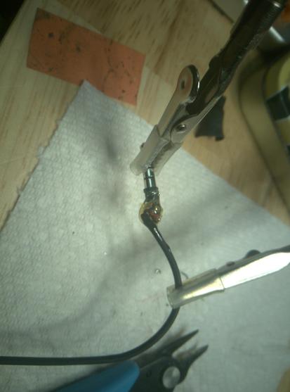 Clips hold a TRRS plug in place. Four tiny wires are soldered onto the rings. A yellow goop covers the entire assembly. A towel, pliers and other misc junk litter the background.