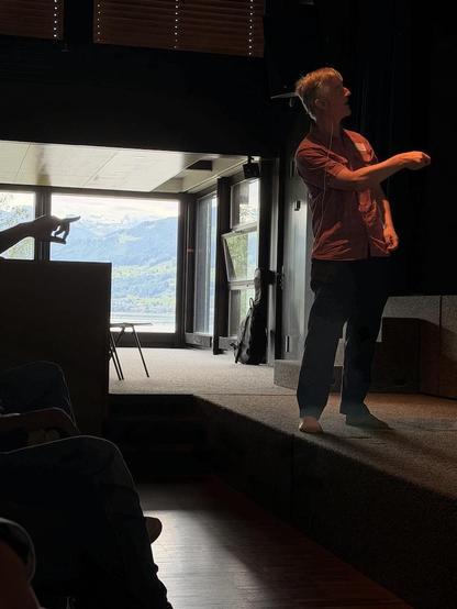 Photo of Simon Peyton Jones in a lecture hall with Lake Zurich and mountains in the background.