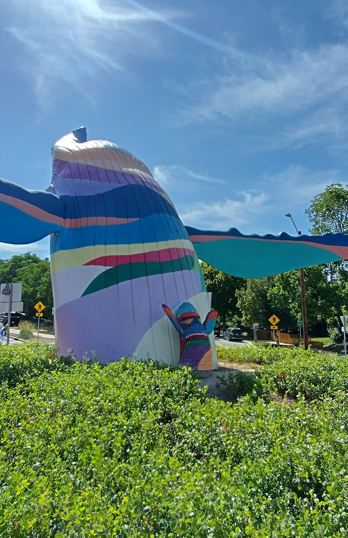 A large, colorful statue of a whale breaching. At the foot of the statue is a smaller copy.