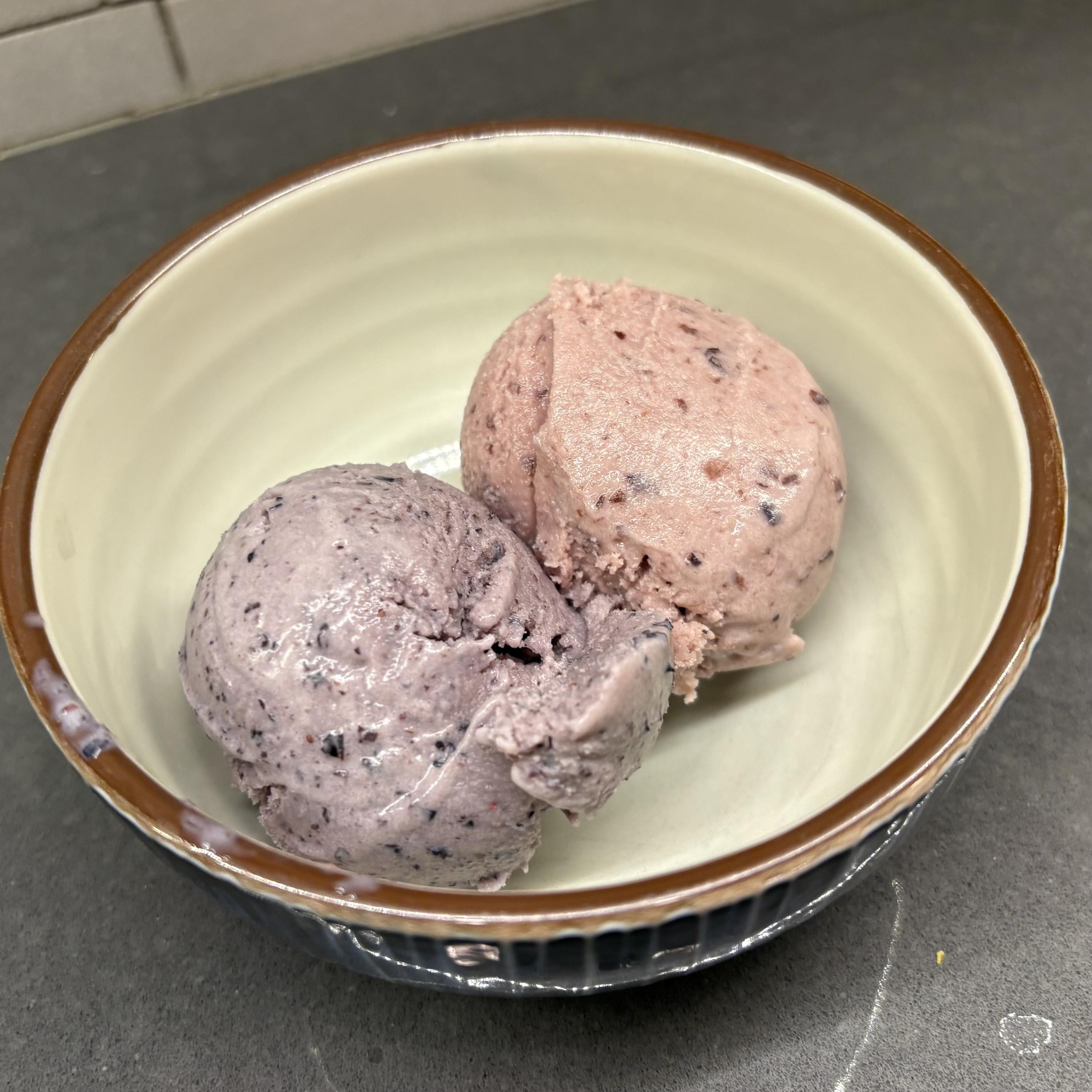 Two scoops of ice cream, blueberry on the left and cherry on the right