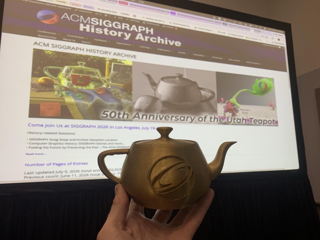 Bonnie Mitchell’s golden 3D-printed teapot, just before it was signed by Jim Blinn, in front of https://history.siggraph.org/, and to be added to the SIGGRAPH History Archive.
